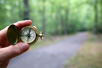 Ein Hand hält einen Kompass auf einem Waldweg.