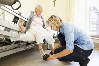 Pflegerin zieht Seniorin Hausschuhe an