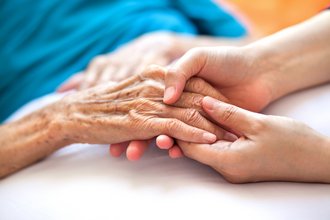 Pflegerin hält Seniorin schützend die Hände