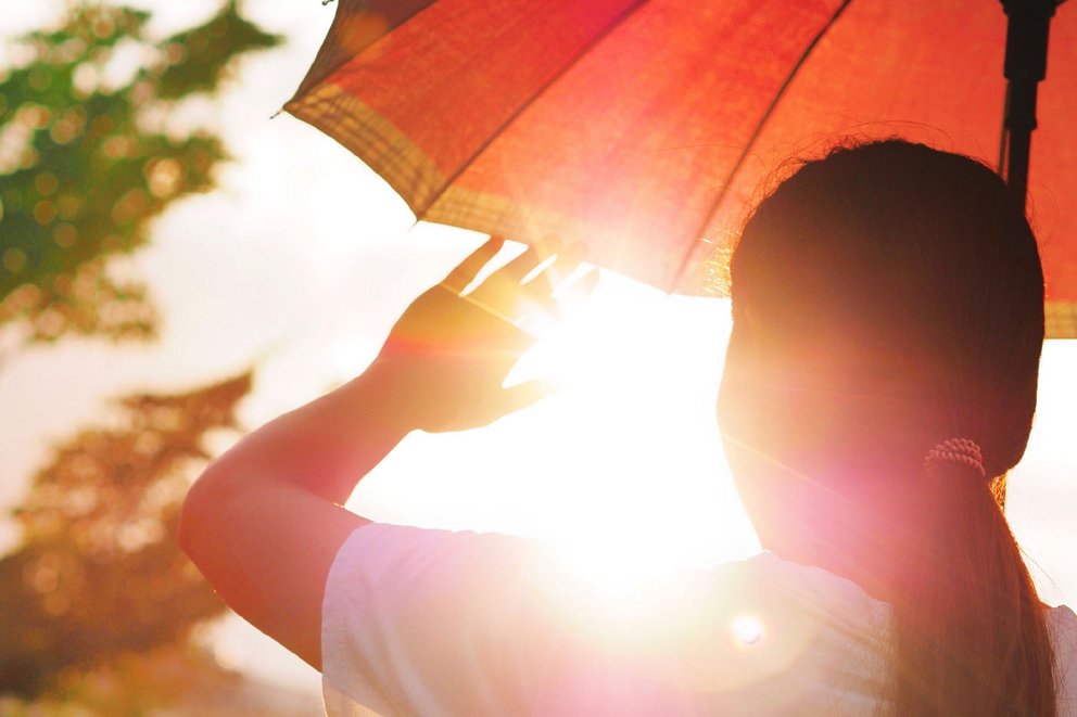Eine Frau hält einen Sonnenschirm und Ihre gehobene Hand vor die Sonnenstrahlen