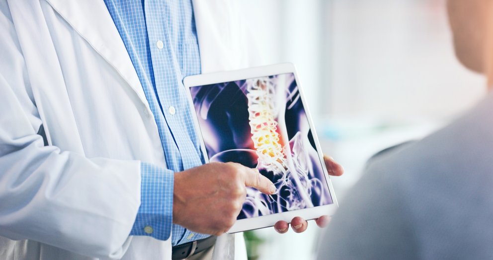 Ein Arzt zeigt einem Patienten ein Röntgenbild der Wirbelsäule auf einem Tablet.