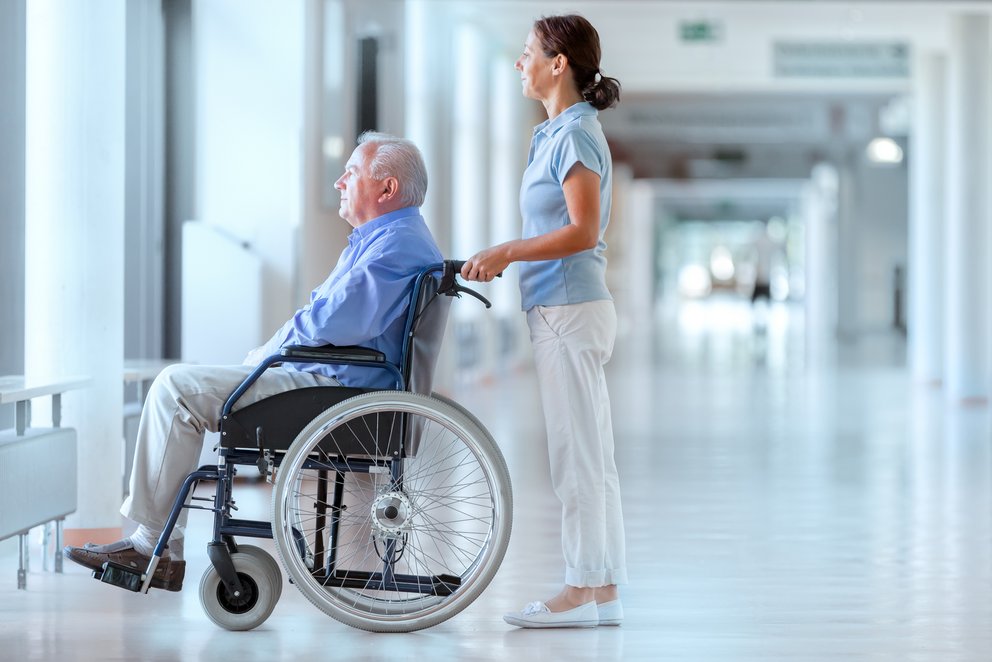 Pflegekraft mit Patient im Rollstuhl im Krankenhaus