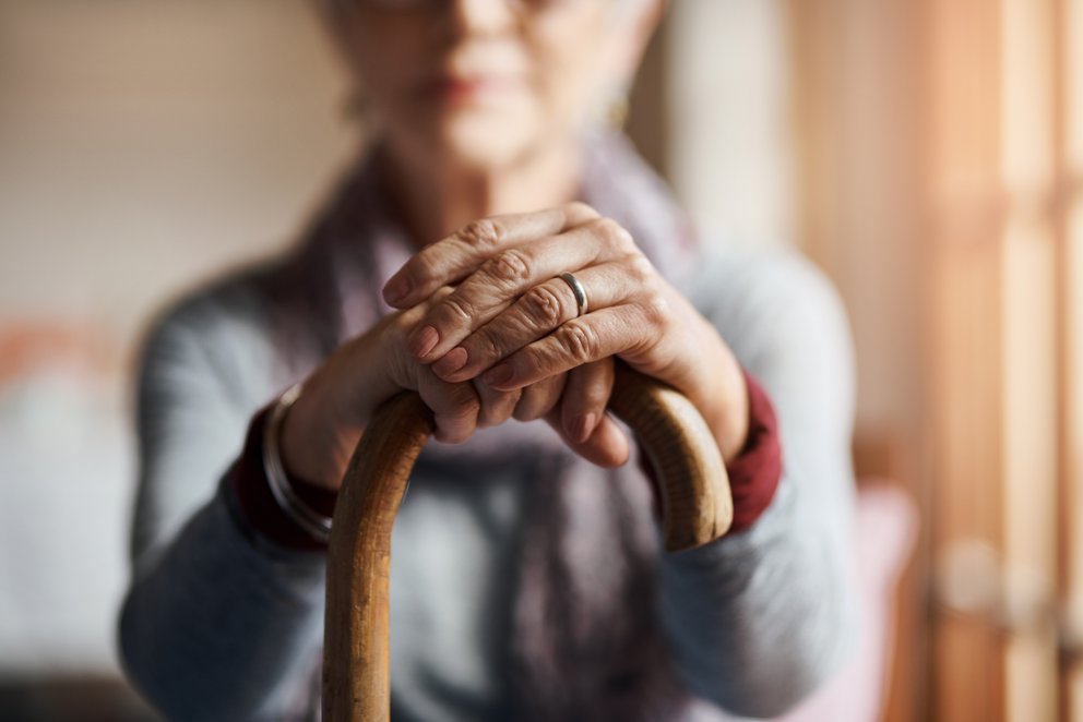 Das Bild zeigt eine alte Dame auf einen Gehstock gebeugt.